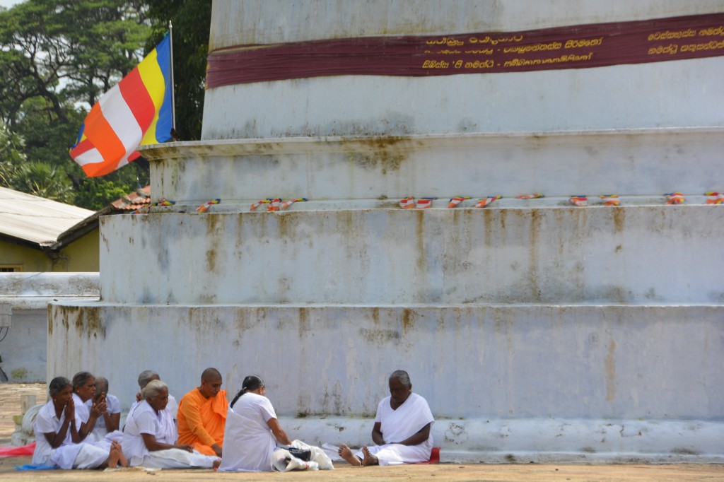 The faithful gather in small groups in the shade of a nearby smaller dagoba