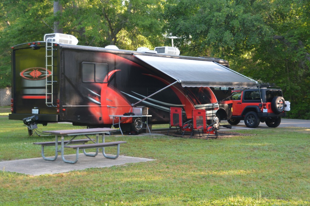 A flash red RV with a matching red jeep and matching red outdoor chairs. In America size does matter.